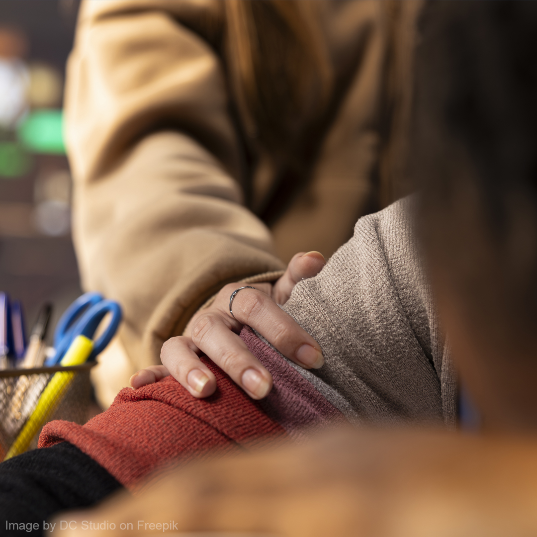 Ein Jugendlicher sitzt auf einer Bank, den Kopf auf der Bank. Eine Schulsozialarbeiterin hockt neben ihm auf Augenhöhe, mit der Hand auf seinem Arm.