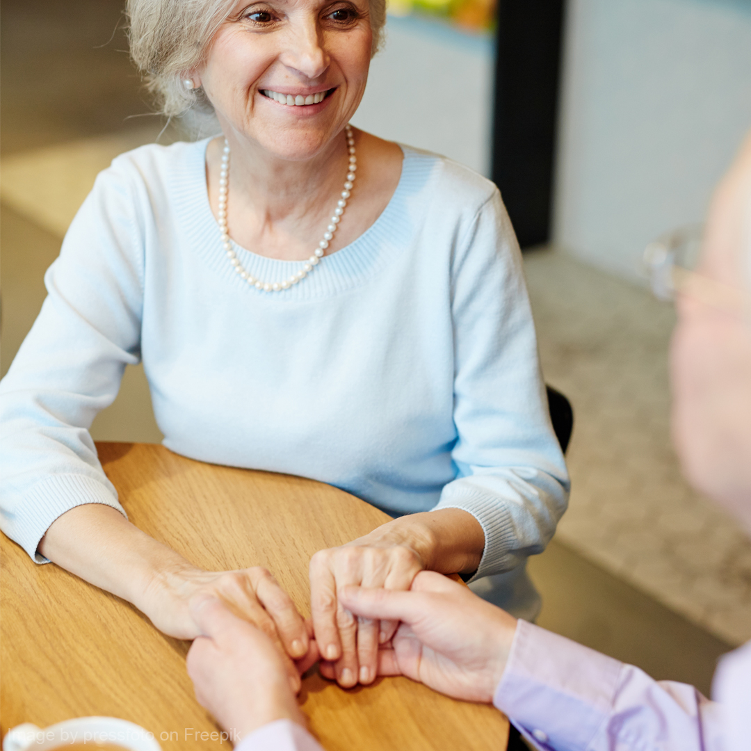 Ein älteres Paar sitzt glücklich am Tisch und hält sich an den Händen.