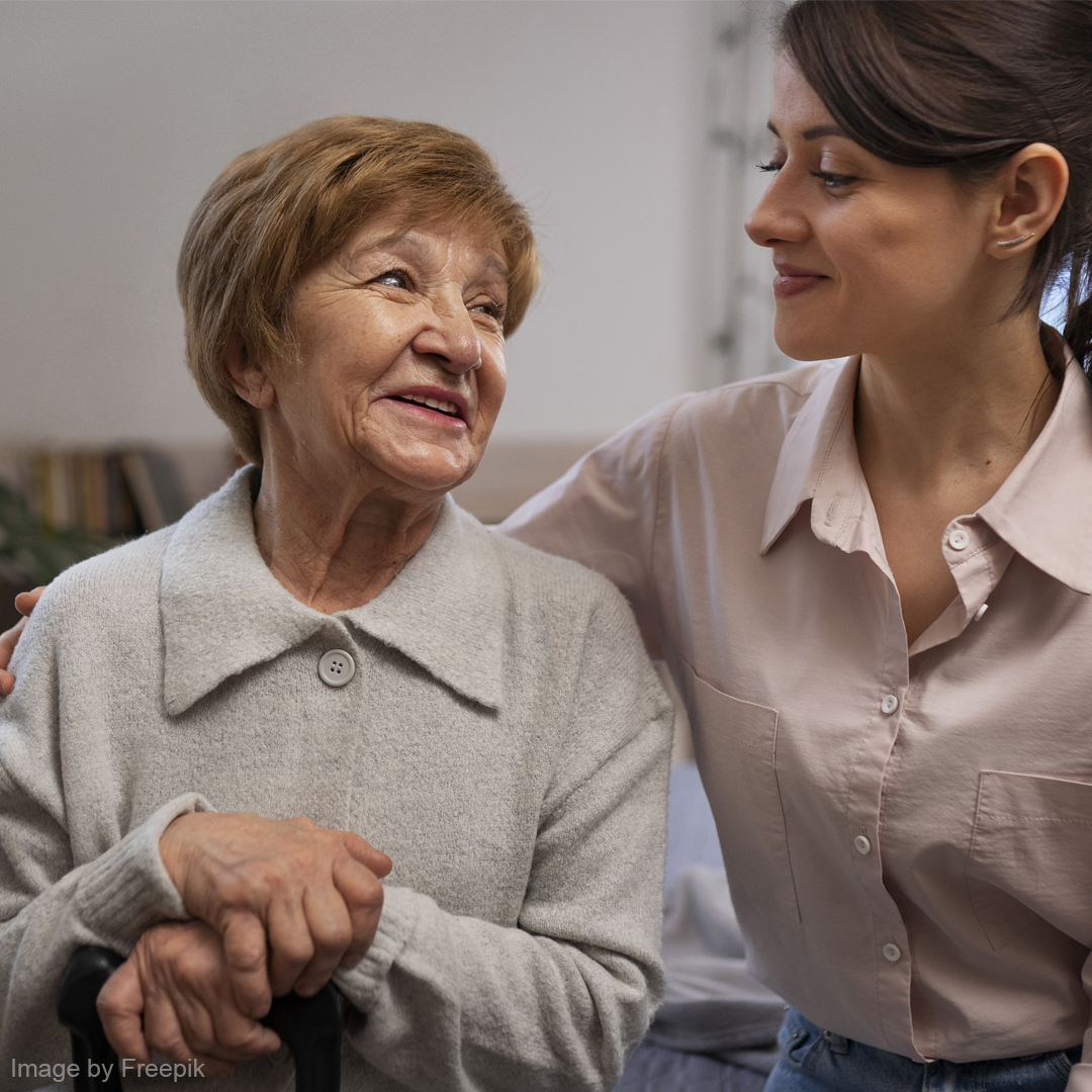 Eine Seniorin sitzt glücklich neben einer Pflegekraft