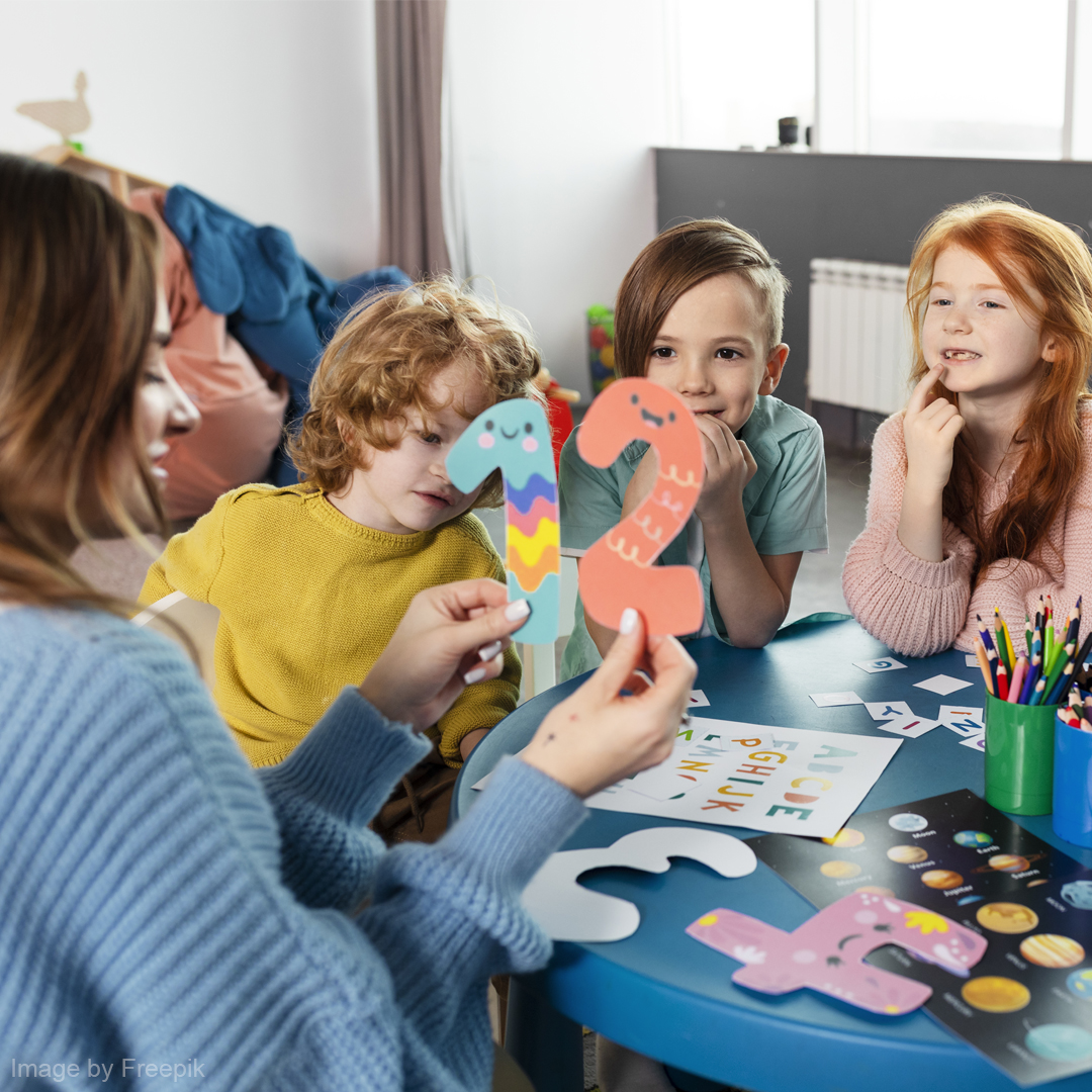 Eine Erzieherin erklärt den Kindern Zahlen und hat dabei 1 und 2 in der hand.